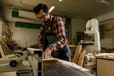 木工车间的作流程服的人在木车间使用加厚刨床专业木工和人的概念车间作流程A挖出工具背景图片