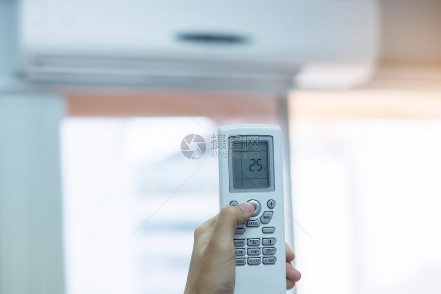家在室内办公或房屋空调机使用手动遥控器调节办公室或房屋内的空调机人们图片