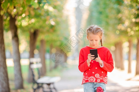 愉快晴天可爱的小女孩在美丽温暖的春日户外手里拿着智能机季节图片
