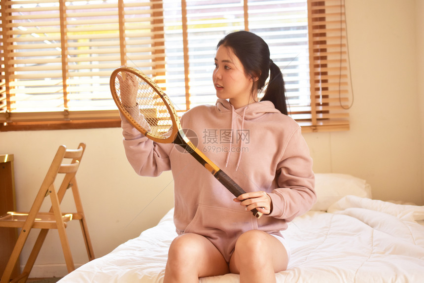 感的妇女坐在卧室床上进行网球拍打妇女坐在房间里人坐在床上她们房间里着单身的图片