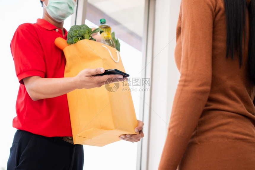 冠状零售亚洲送货员持有一袋新鲜食品供顾客使用并拥有智能手机在家中接收付款快速杂货服务和新生活方式概念a提供快餐服务和新生活方式的图片