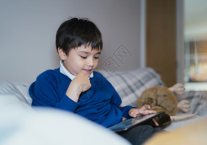 房间乐趣Kid使用互联网向老师发送家庭作业坐在沙发上的孩子放学后独自客厅休息下课后单独坐沙发上放松一下的孩子们校友触碰背景图片