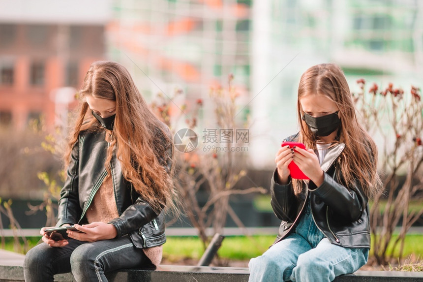 为了身戴面具在户外防止和玩智能手机保护游戏以防止Corona和抓风的女孩身戴面具防止Corona和抓网的小女孩大流行移动的图片