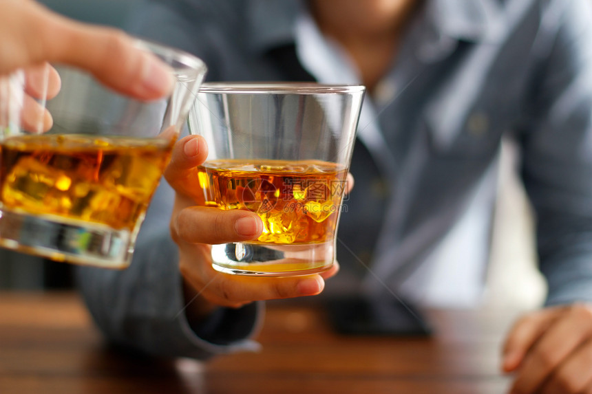 在酒吧的柜台时一起喝着威士忌酒精饮料杯子上两个男人的紧贴杯子敬酒工人吸引的图片