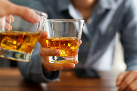 叮叮当当在酒吧的柜台时一起喝着威士忌酒精饮料杯子上两个男人的紧贴杯子敬酒工人吸引的背景