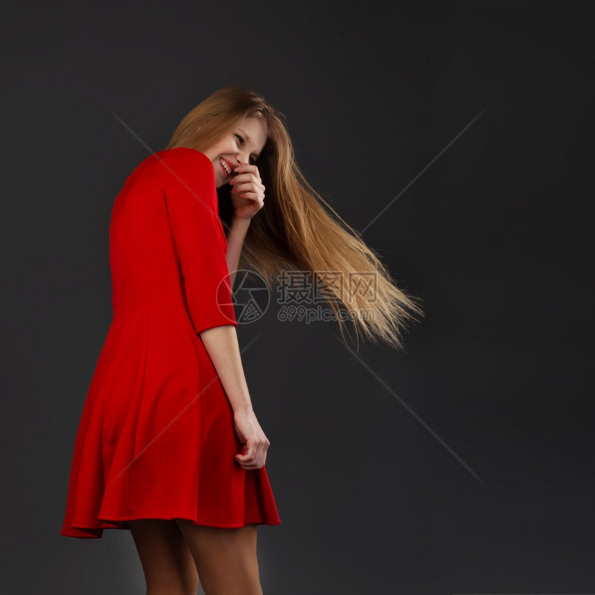 一个笑的年轻漂亮女孩肖像穿着红色礼服与一个飞着头发的姑娘长卷的姑娘后退关心美丽的图片