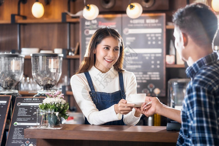 喝牛奶亚洲小企业主律师协会在咖啡店柜台向青年顾客提供一杯咖啡小商业主和咖啡店餐馆的创办人概念小型商业主亚洲协会为咖啡店和餐馆的年图片