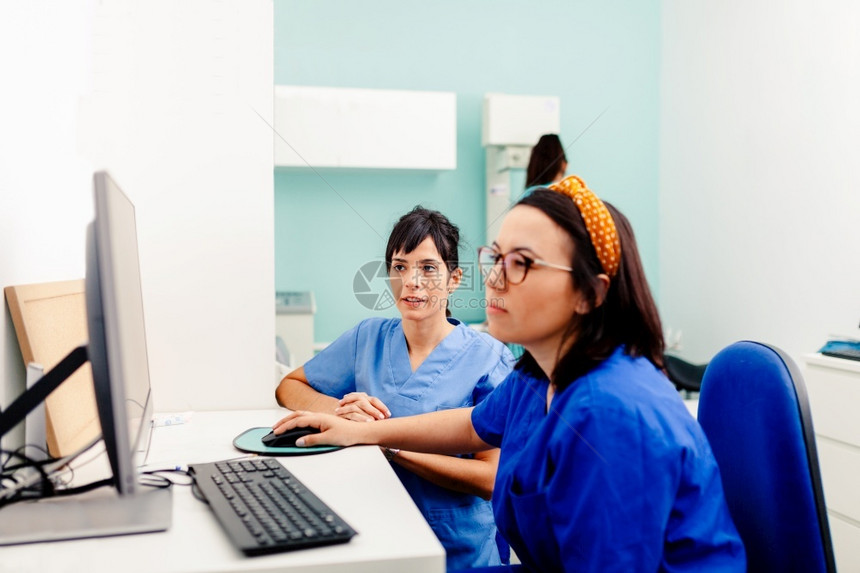 X射线职业两名护士在X光室使用计算机其中一名佩戴眼镜坐在书桌附近2名护士在X光室使用计算机2名护士在X光室使用计算机桌子图片
