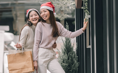 在圣诞节新年庆典和销售折扣概念中两个可爱的妇女在百货店买窗户时拿着袋子在圣诞季新年庆祝和销售折扣概念喜悦城市笑背景图片