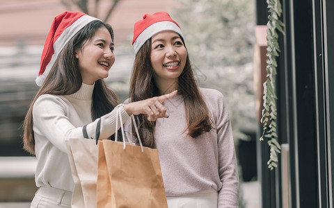 在圣诞节新年庆典和销售折扣概念中两个可爱的妇女在百货店买窗户时拿着袋子在圣诞季新年庆祝和销售折扣概念女孩们服装顾客背景图片