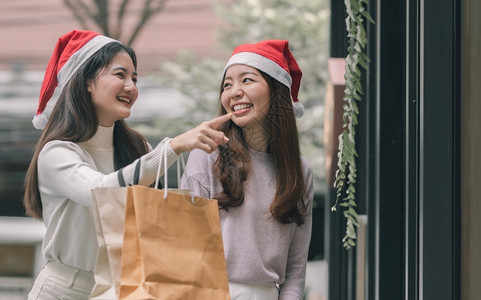 购物狂市场女在圣诞节新年庆典和销售折扣概念中两个可爱的妇女在百货店买窗户时拿着袋子在圣诞季新年庆祝和销售折扣概念背景图片
