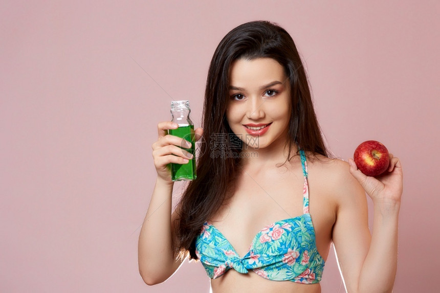 福利饮食身穿泳衣的年轻苗头亚洲女孩带着新鲜果汁和苹在手上微笑粉红孤立的背景上笑热带图片