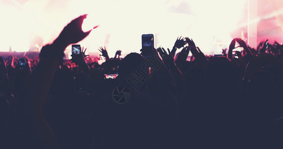 岩石声音明亮的舞台灯下举起手来在音乐会观众看节日人群的后视线上欢呼背景图片