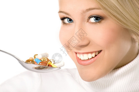 营养的美丽颜色金发笑着的金发美女蓝眼睛在勺子上吃了很多丰富彩的药丸图片