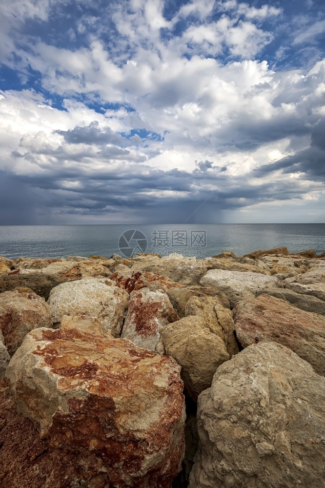 海岸上多彩的石头地平线垂直视上有暴云极好的美丽景图片