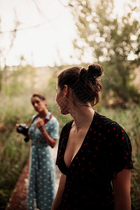 现代的年轻两个女子在森林里拍相照身穿礼服和运动鞋的树上拍照白天图片