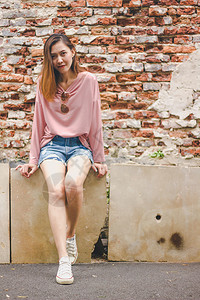 金发女郎年轻的一个人靠着堵旧砖墙她穿粉红衬衫色的图片