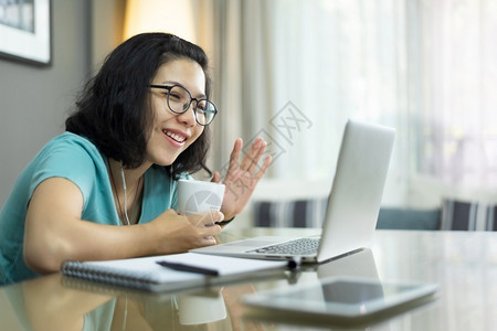 年轻的无线有吸引力亚洲妇女用笔记本电脑和手挥打视频电话身着蓝衬衫的年轻女在家庭网上电子学习和中通过互联网技术与家人和民众交谈穿着亚洲人高清图片素材