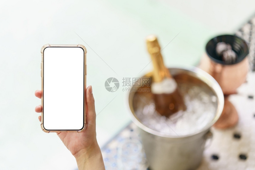 蜜月妇女手握空白屏幕移动电话在冰桶里装香槟瓶在按摩池附近有两杯玻璃水池靠近图片