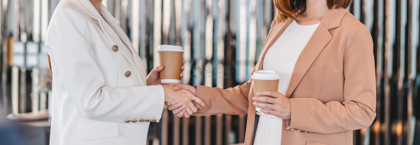 办公室在成功伙伴商业协议成功时两名手握咖啡纸杯和手的亚裔女实业商人与完成交易的小企业一起达成功的合作伙伴商业协议后完成了交易概念图片