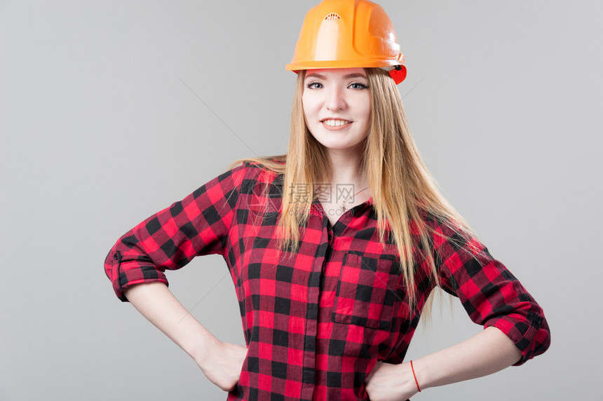 安全帽成人一个年轻有魅力的女人金发橙色头盔格子衬衫中灰色背景一个年轻有魅力的女人中灰色背景年轻的图片