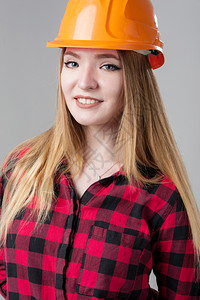 一个年轻有魅力的女人金发橙色头盔格子衬衫中灰色背景一个年轻有魅力的女人中灰色背景专业的帽子设计师背景图片