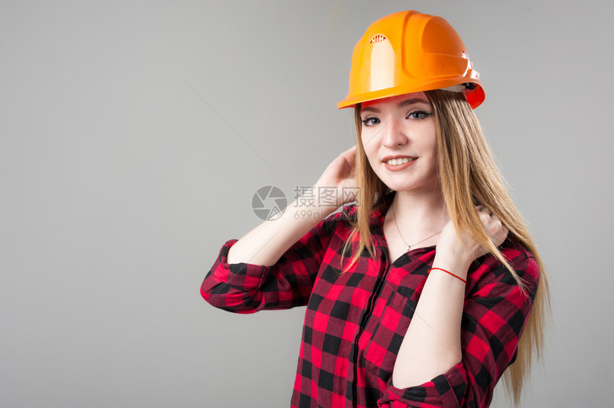 工程建设者一个年轻有魅力的女人金发橙色头盔格子衬衫中灰色背景一个年轻有魅力的女人中灰色背景设计师图片