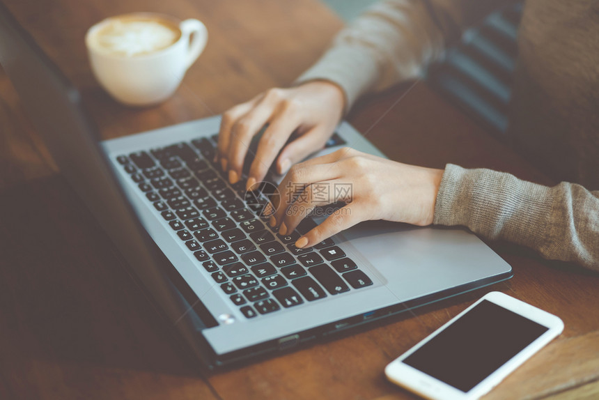 研究作家木头利用计算机笔记本电脑和移动智能话工作的妇女自由职业者在一家咖啡厅店的木桌上用咖啡杯送工作的妇女图片