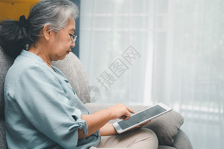 诫子书无线的高级亚洲妇女戴眼镜在家沙发上放松并使用平板电脑阅读新闻和子书老年人技术概念为老年人提供技术概念成熟高级的背景