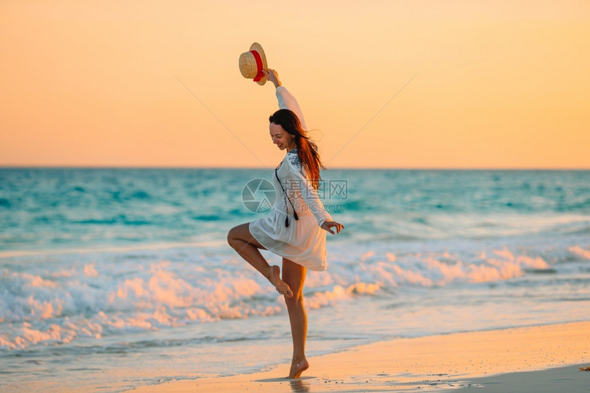 放松水异国情调在日落的热带海滩上年轻的美丽女人在黄昏的热带海滩上年轻漂亮的女孩在美丽着装背景的年轻女孩后视中图片
