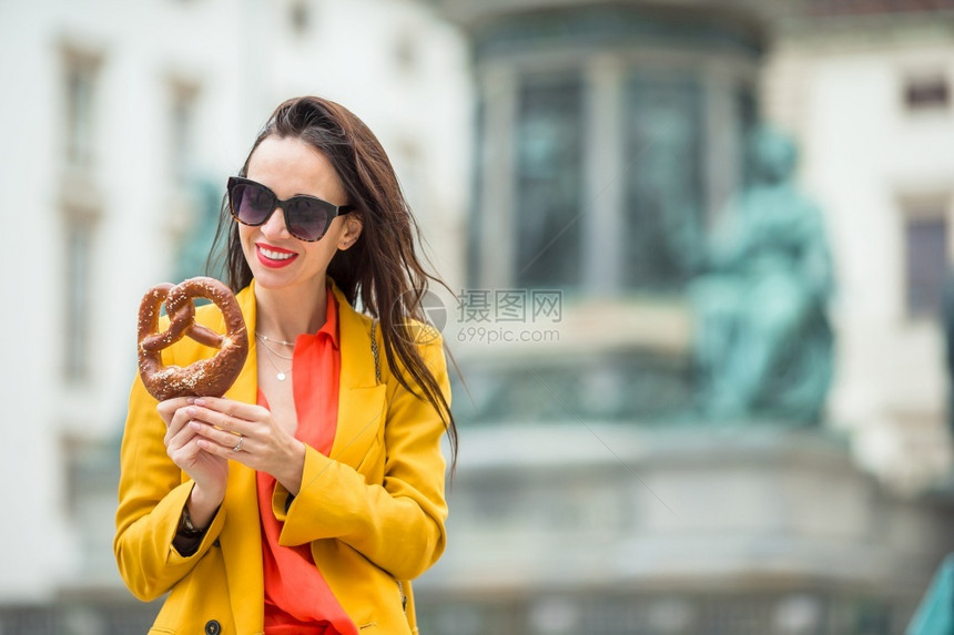 节日美丽的年轻女子拿着椒盐卷饼在欧洲的公园里放松时尚旅行图片