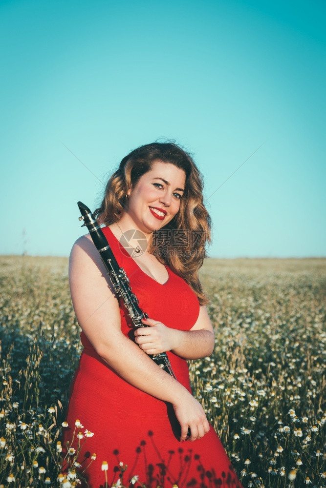 音乐家穿着红裙子的女人在田里玩着单簧管风白种人图片