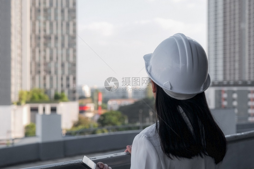 职业在建筑工地带平板电脑的女建筑工程师戴着白色头盔的自信女建筑师看着工地和概念微笑成功图片