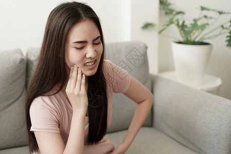 沙希辛达衰变病人敏感的亚洲妇女在家里坐沙发上时有牙痛亚洲女孩脸上的表情达方式是牙痛和科药物亚洲妇女有牙痛背景