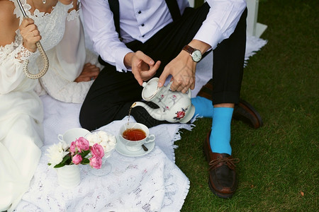 雨新娘和郎在绿草上盛着鲜亮的衣服喝茶套装手图片