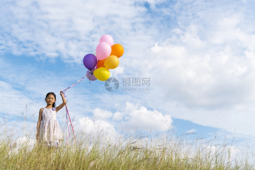 快乐的可爱女孩拿着气球在绿色草地白云和蓝天空上运行快乐的天空手拿着充满活力的空气球在生日派对上玩欢乐的可爱女孩士假日束图片