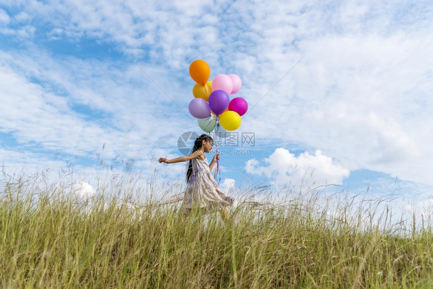 太阳快乐的可爱女孩拿着气球在绿色草地白云和蓝天空上运行快乐的天空手拿着充满活力的空气球在生日派对上玩欢乐的可爱女孩子图片