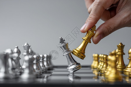 实战营帕努瓦团队在棋盘竞争战略成功管理商业规划中断和领导力概念期间商人用手搬运金牌象棋王人物和格斗士或对手的实战人数木板背景