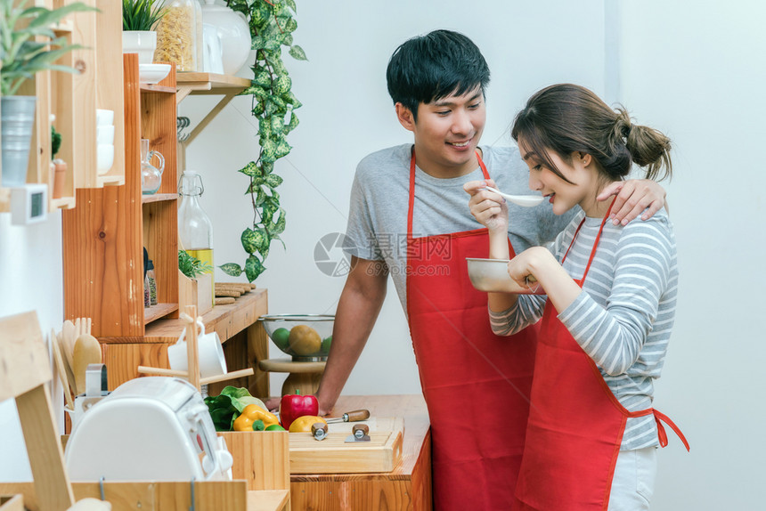 亚洲情人或侣烹饪和在现代房子夫妇和生活方式概念的厨房里尝着食物并享受到品已婚一顿饭玩图片