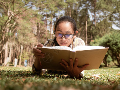 夏天笔记本年轻亚洲女在度假日放松并阅读一本躺在花园的草地上书随意图片