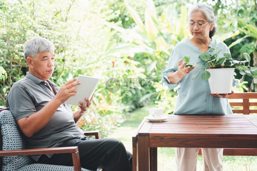 花男一位快乐和笑的亚洲老年妇女在退休后为业余爱好植树她的丈夫正在读一本书老年人幸福生活方式和健康概念一老年人幸福和健康的概念家庭图片