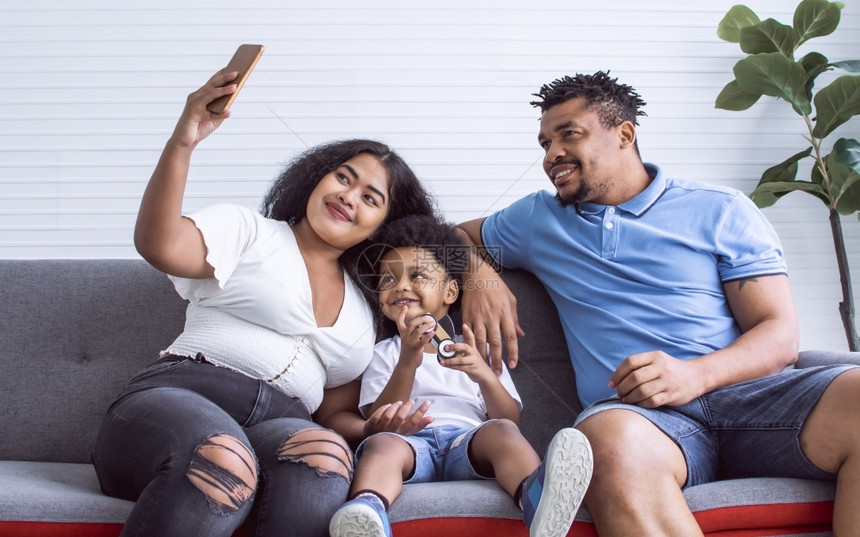 非洲家庭使用手机自拍坐在家用沙发上生活风格概念LivestyleNeption坐着微笑为人父母图片