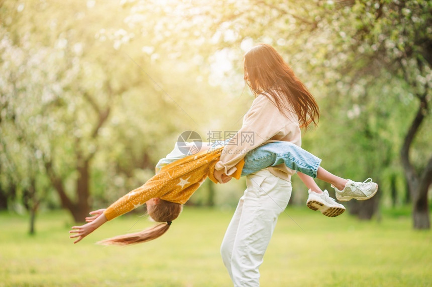 快乐的母亲和女儿家庭在公园户外玩得开心在盛的樱花园中母亲和女儿家庭年轻的季节图片