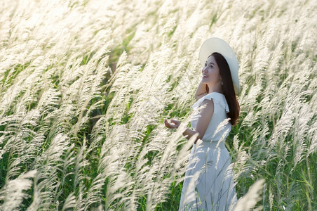 自由梦幻般的白色草地上花她裙子和白帽站在色草原上的地PrachuapKhiriKhan泰国美丽的天然白草地花头发背景图片