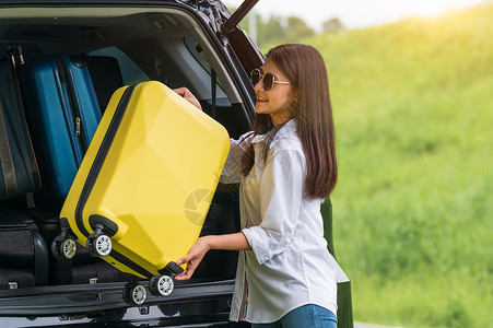 长途旅行妇女将黄色手提箱抬上SUV车图片
