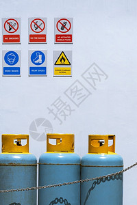 抽烟制造在安全区白色水泥墙上挂有各种警告标志的气罐瓶图片