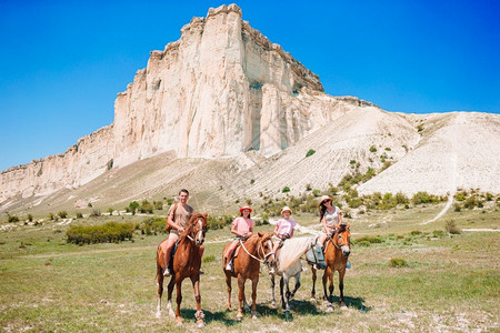 家庭骑马在岩石和山峰背景上欢乐的四口家庭日落时在山上行走马背匹骑术图片