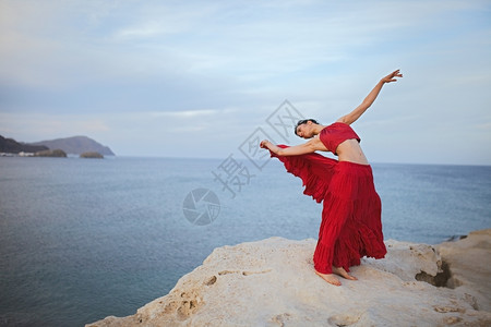 身穿红礼服的黑发年轻女人在海滨附近岩石上跳舞女享受卵石图片