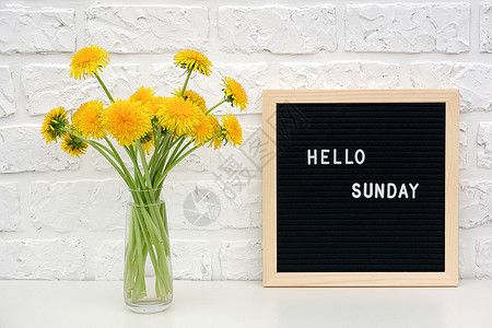 你好星期天黑色字母板上的单词和桌子黄色蒲公英花束图片