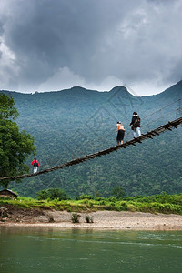 学校超过风暴一群老挝高中女生穿过南宋河上简单的悬吊脚桥在北老挝农村背景的山上云雾笼罩着巨大黑暗位于北老挝农村地区背景图片